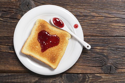 Toasted bread with strawberry jam in the shape of heart in plate on old wooden table, top view